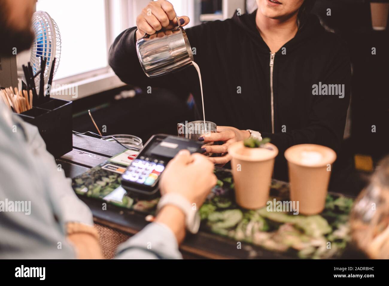 Kunden im Gespräch mit weiblichen Barista während Kaffee im Cafe kaufen Stockfoto