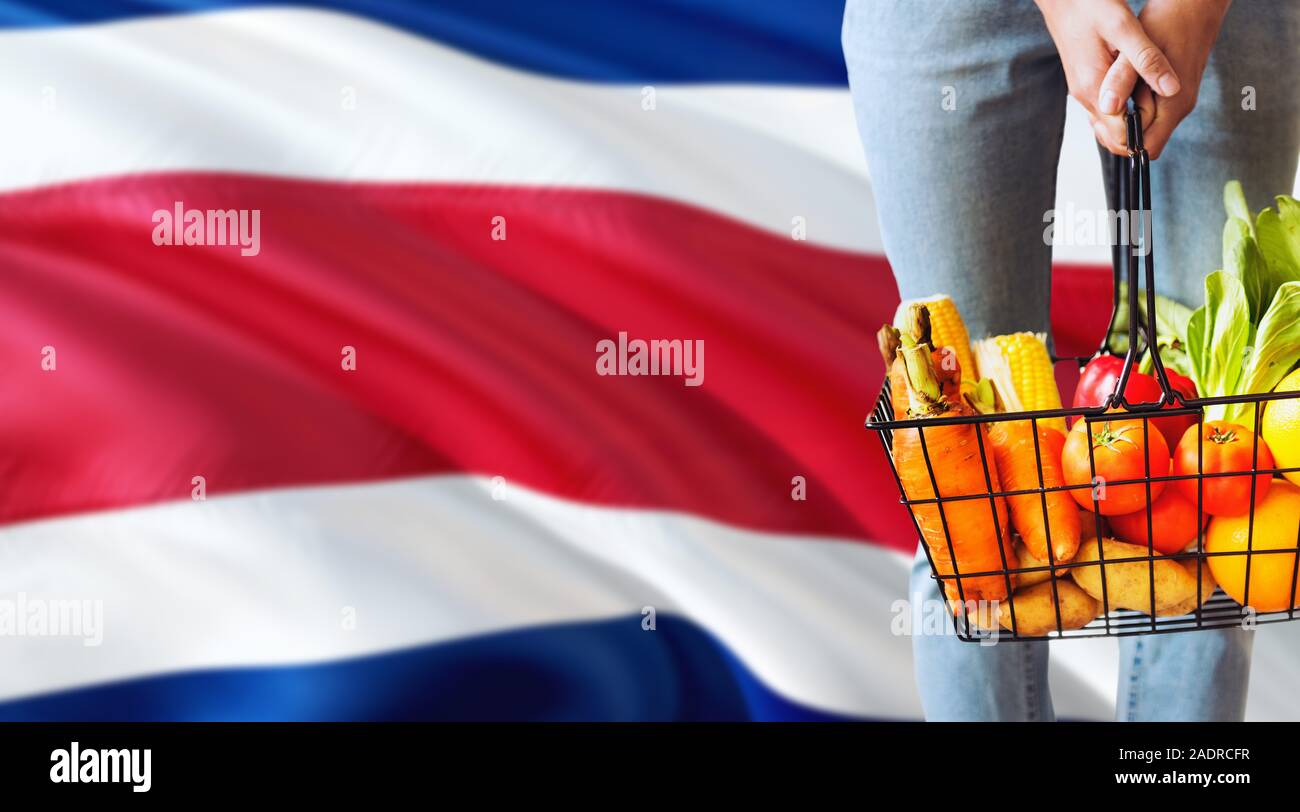 Frau hält Supermarkt Korb, Cote D'Ivoire wehende Flagge Hintergrund. Wirtschaft Konzept für frisches Obst und Gemüse. Stockfoto