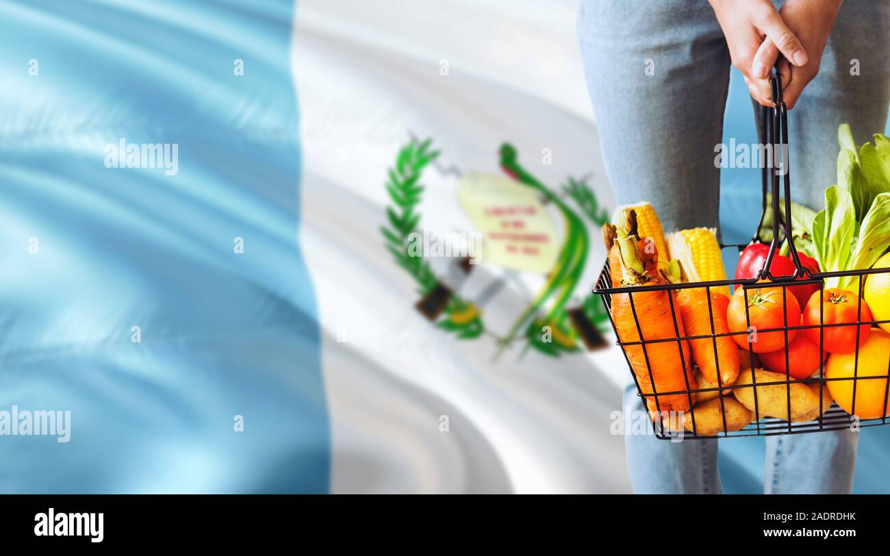 Frau hält Supermarkt Korb, Guatemala wehende Flagge Hintergrund. Wirtschaft Konzept für frisches Obst und Gemüse. Stockfoto