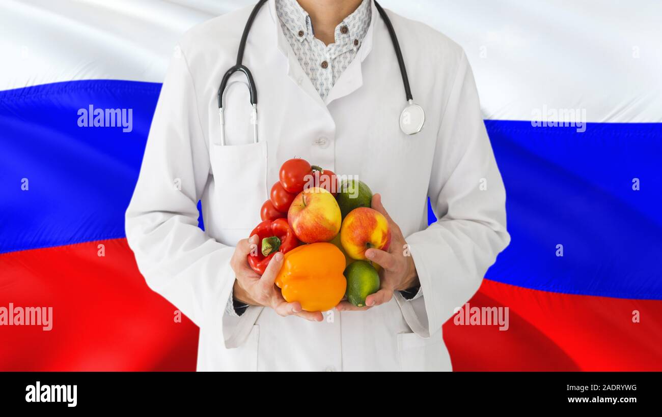 Arzt hält Obst und Gemüse in den Händen mit Russland Flagge Hintergrund. Nationalen Gesundheitswesen Konzept, medizinische Thema. Stockfoto