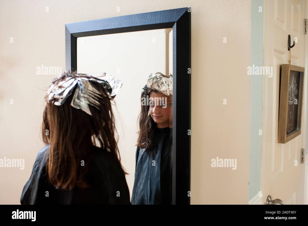 Tween Mädchen an ihr Spiegelbild auf der Suche mit Folien aus Haaren Highlights Stockfoto