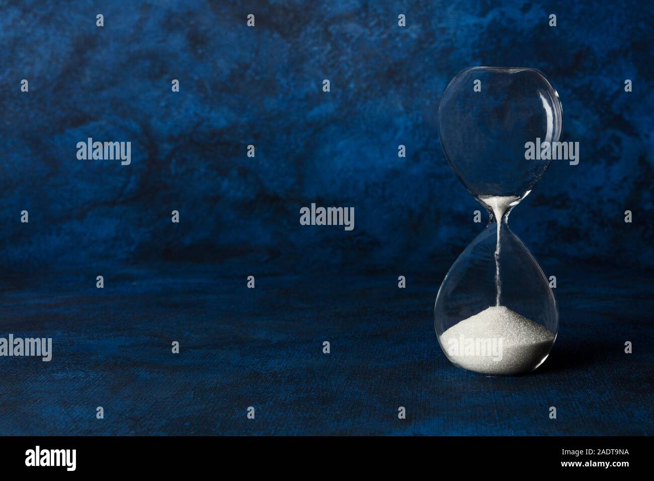 Die Zeit läuft. Eine Sanduhr mit nässen Sand, auf dunkelblauem Hintergrund mit Kopie Raum Stockfoto