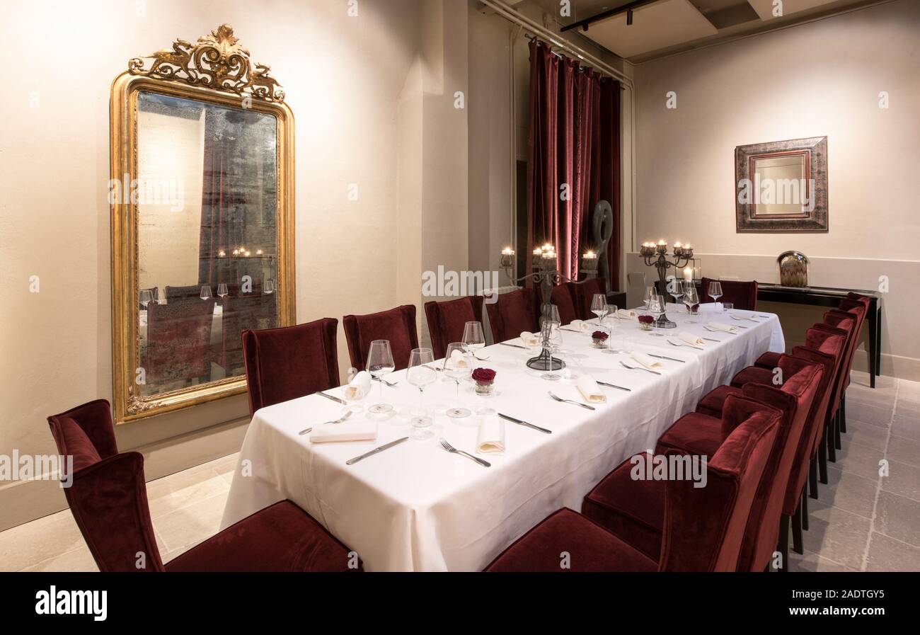 Langer Tisch zum Abendessen in einem Restaurant mit elegantem Interieur mit vergoldeten Spiegeln und Samtvorhängen eingestellt Stockfoto