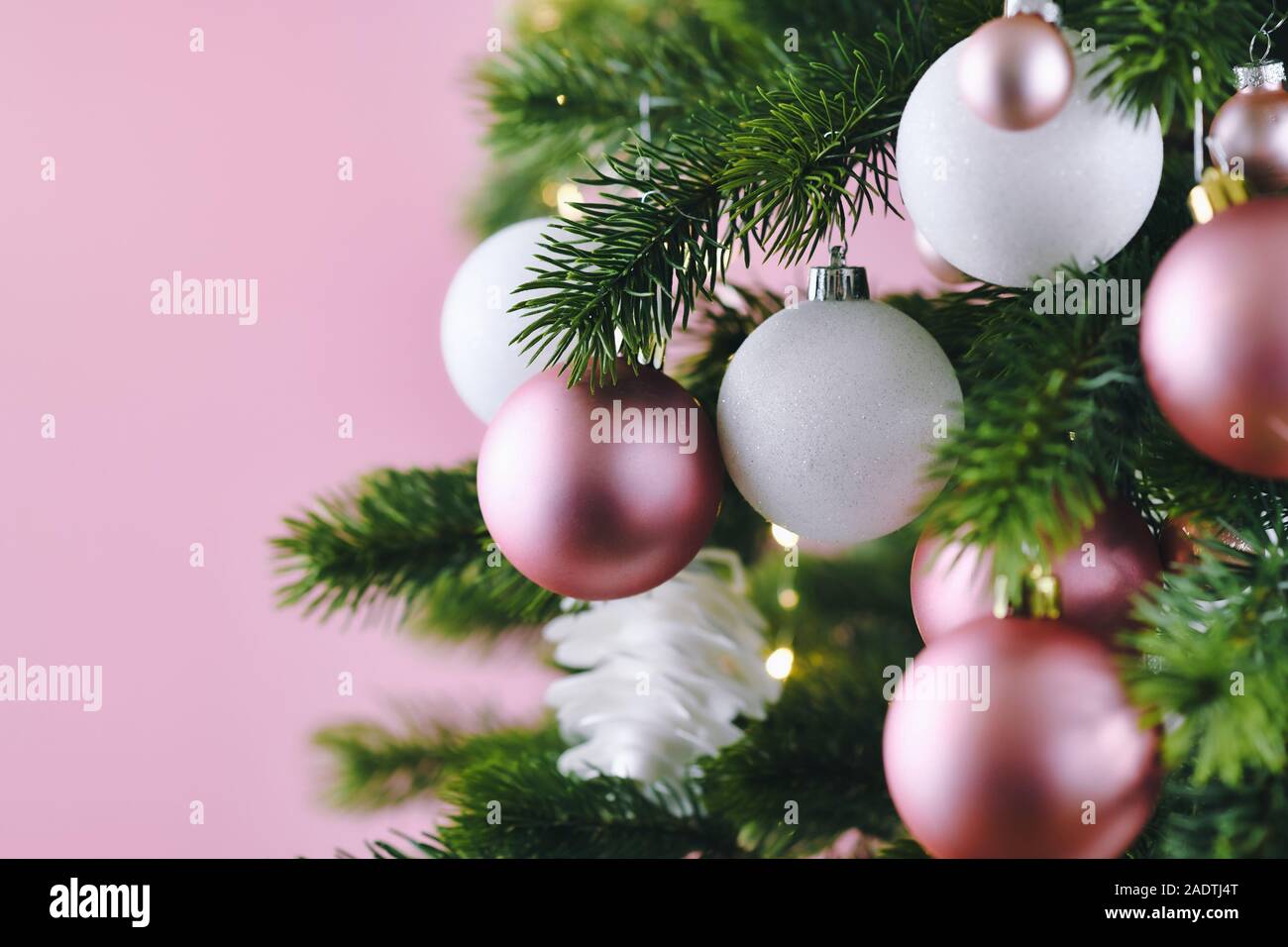 Nahaufnahme von geschmückten Weihnachtsbaum mit weißen und rosa Saison baumschmuck wie Kugeln und Sterne auf rosa Hintergrund mit Licht im Hintergrund Stockfoto