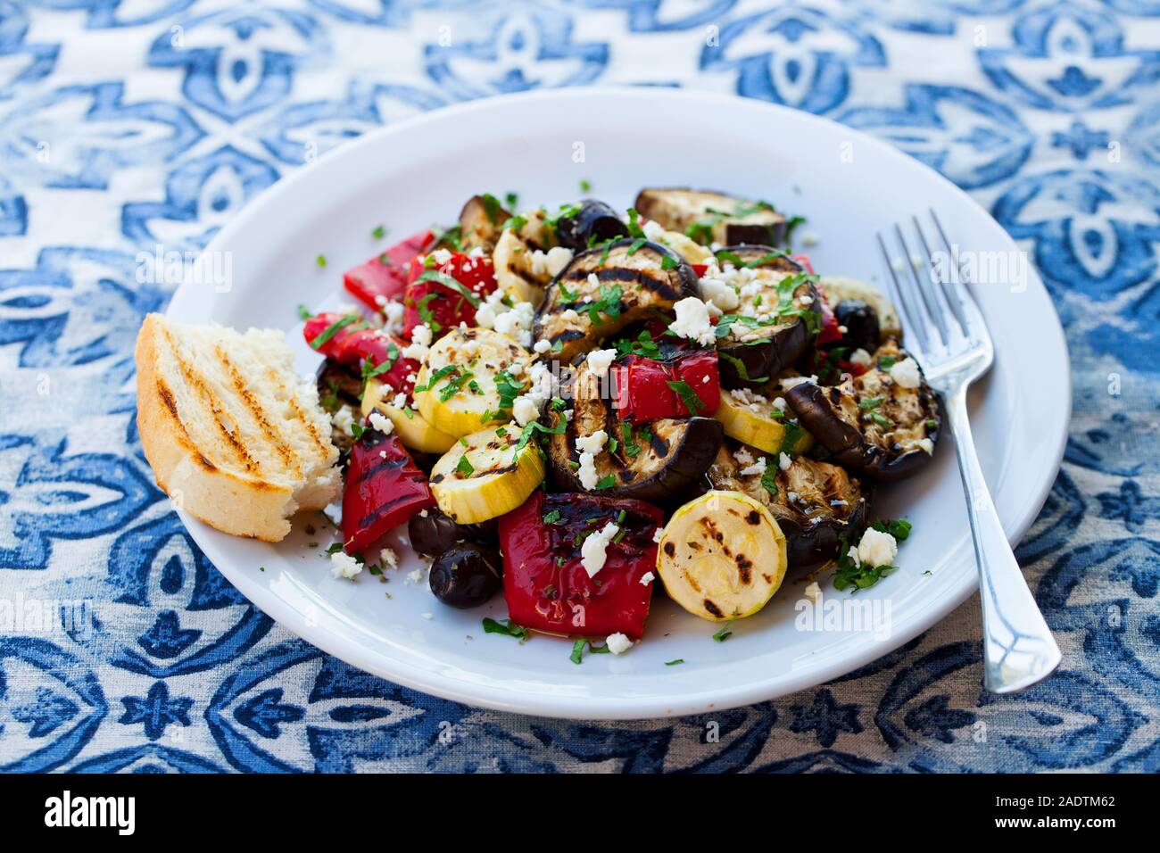 Gegrilltes Gemüse Salat mit Feta Käse in weiße Platte auf Blue Background. Nahaufnahme Stockfoto