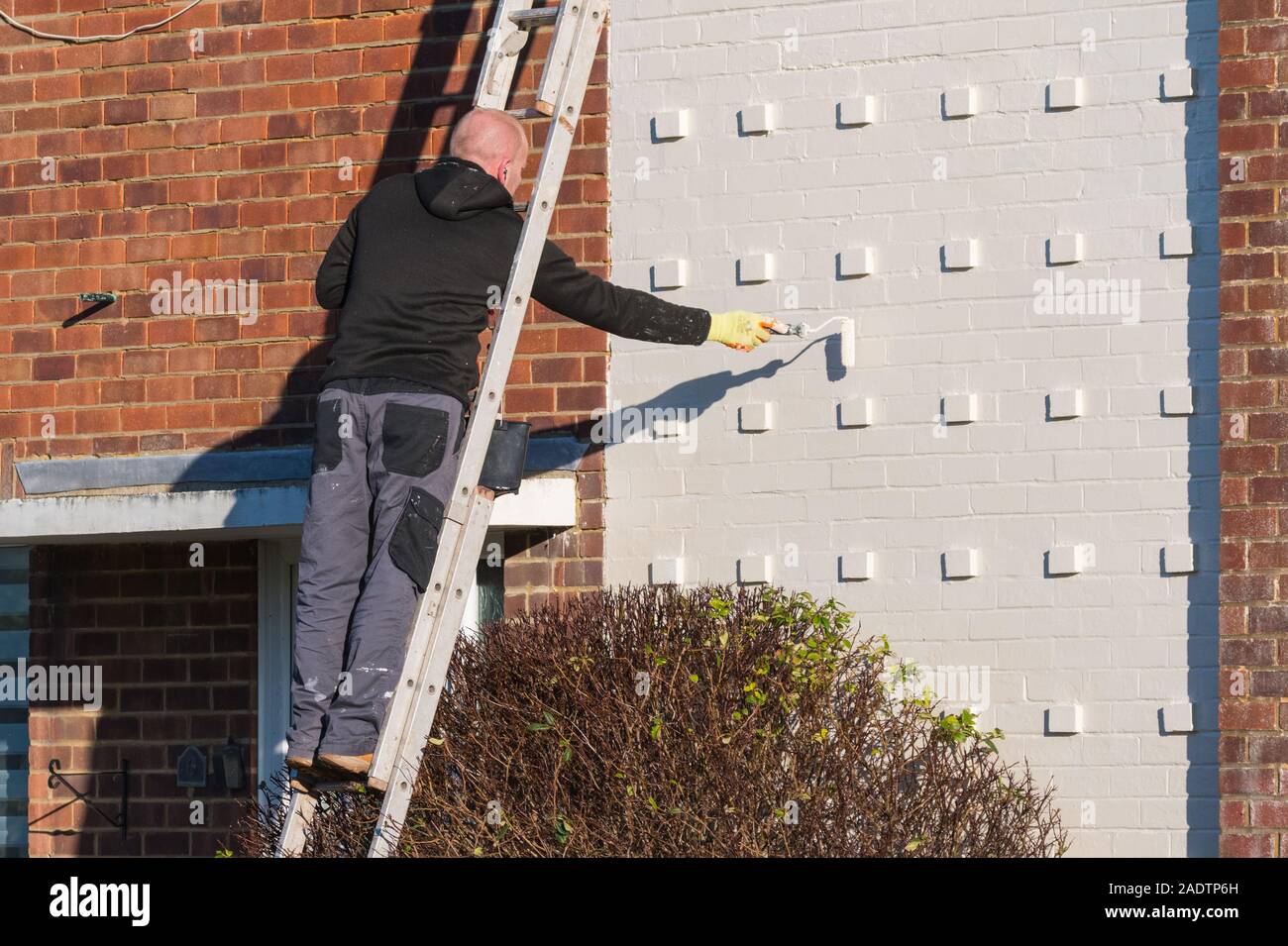Mann auf eine Leiter Malerei und die Dekoration der Fassade eines Hauses mit einer Bürstenrolle. Stockfoto