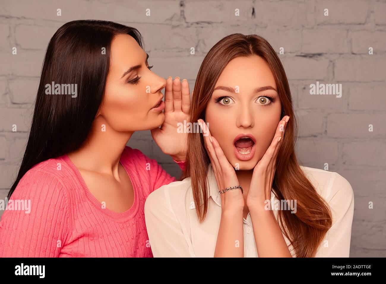 Schöne Mädchen sagt der Klatsch in das Ohr von ihr überrascht Freundin Stockfoto