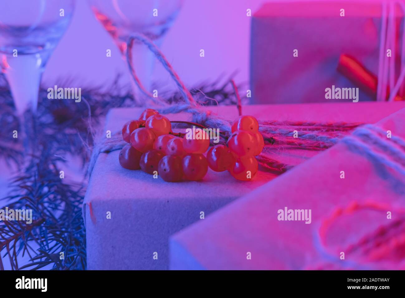 Weihnachtsgeschenke in nachhaltiger Verpackung in Neonlicht. Neujahrsparty-Konzept: Geschenke, Getränke und Gläser in rosa und blau Hintergrund Stockfoto
