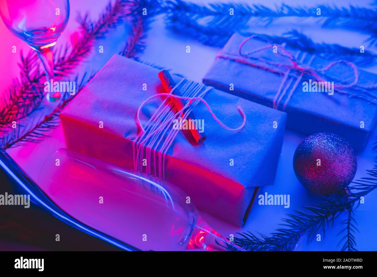Weihnachtsgeschenke in nachhaltiger Verpackung in Neonlicht. Neujahrsparty-Konzept: Geschenke, Getränke und Gläser in rosa und blau Hintergrund Stockfoto