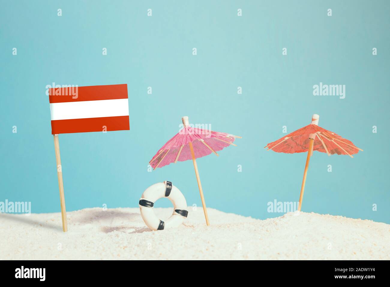 Miniatur Flagge Österreich am Strand mit bunten Sonnenschirmen und Schwimmweste. Travel Concept, Sommer Thema. Stockfoto