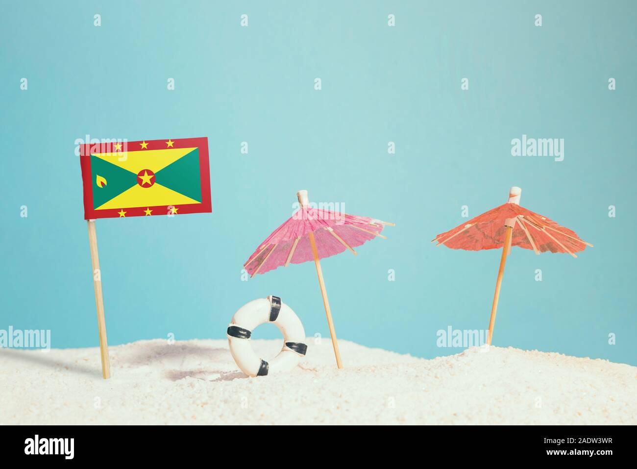 Miniatur Flagge Grenada am Strand mit bunten Sonnenschirmen und Schwimmweste. Travel Concept, Sommer Thema. Stockfoto