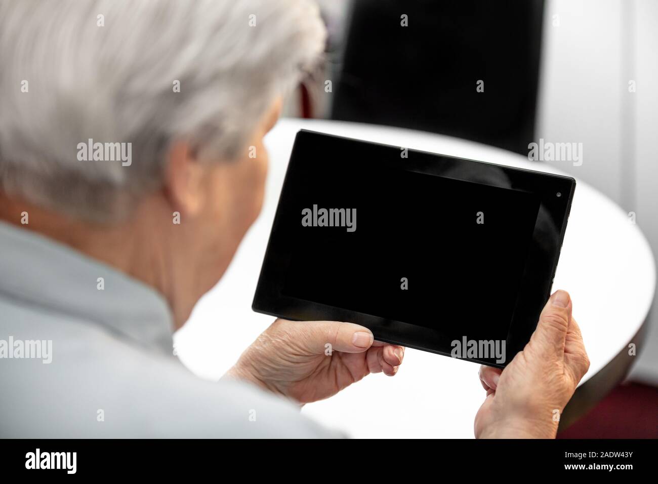 Moderne Oma am Schreibtisch auf der Suche von einer Tablette mit Copyspace, ältere Frauen und Computer Technologie Stockfoto