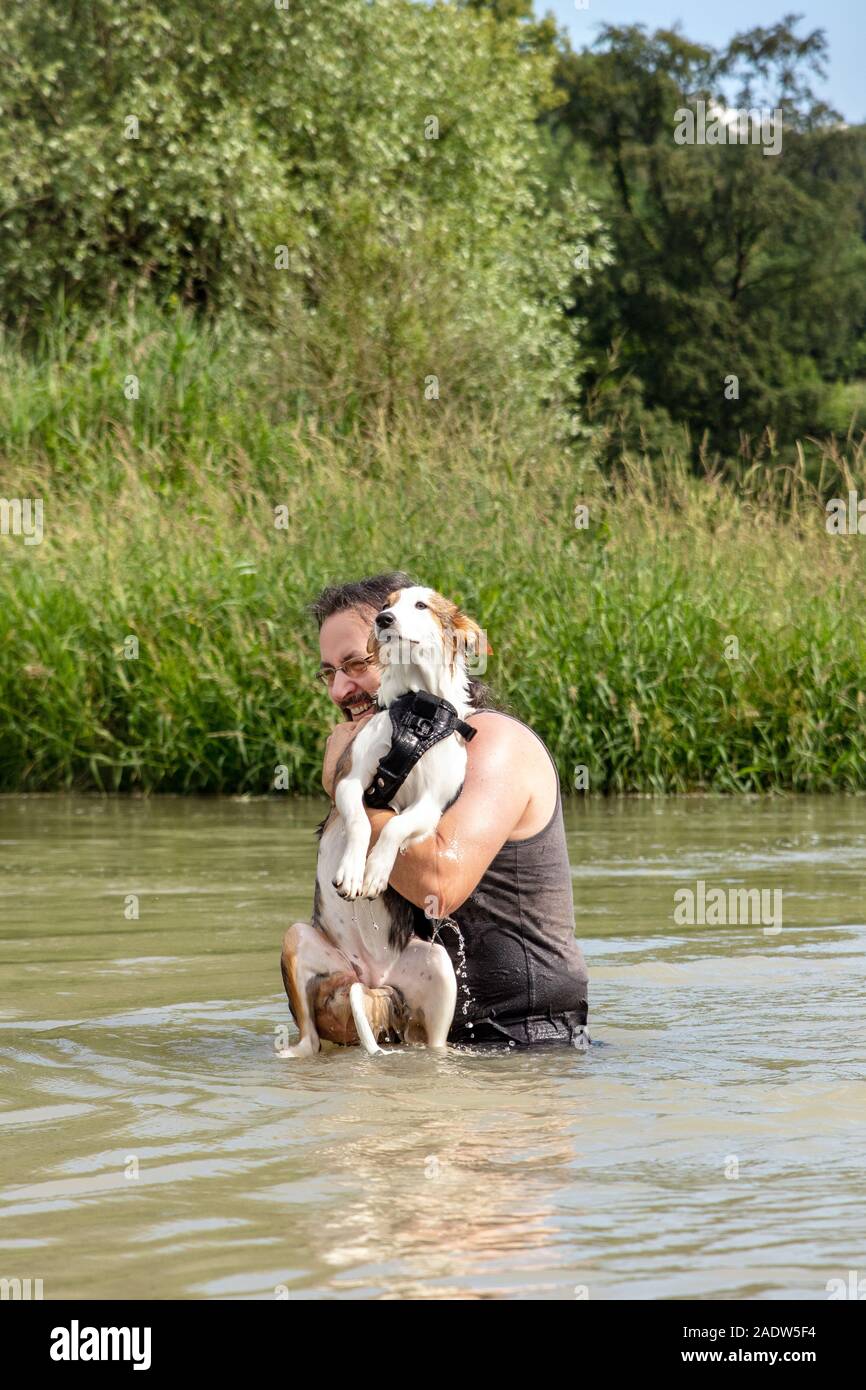 Mann, der in einen See und seinem jungen Hund, Gehorsam und Trainee Holding mit Wasser Stockfoto