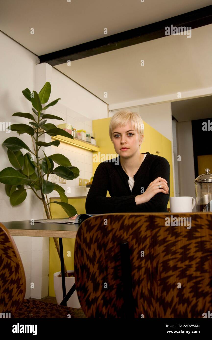 Eine junge Frau, die zu Hause in Ihrer Küche mit einer Zeitung und Kaffee auf den Tisch vor ihr entspannend. Stockfoto