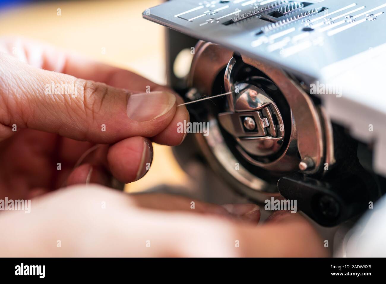 Hand eines Mannes ist Threading ein Thread auf den Nähfuß seiner Nähmaschine Stockfoto