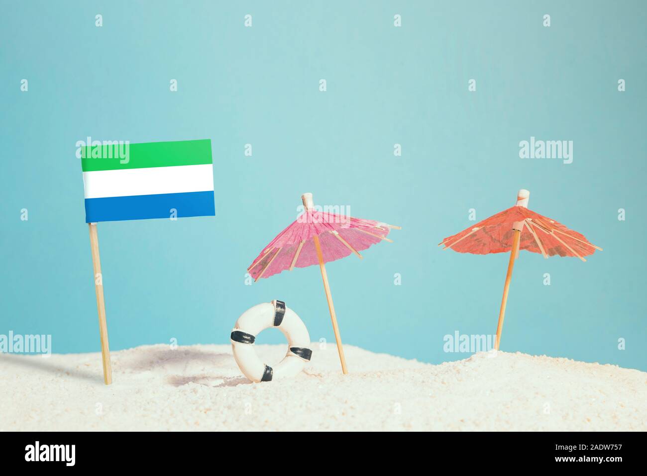 Miniatur Flagge von Sierra Leone am Strand mit bunten Sonnenschirmen und Schwimmweste. Travel Concept, Sommer Thema. Stockfoto