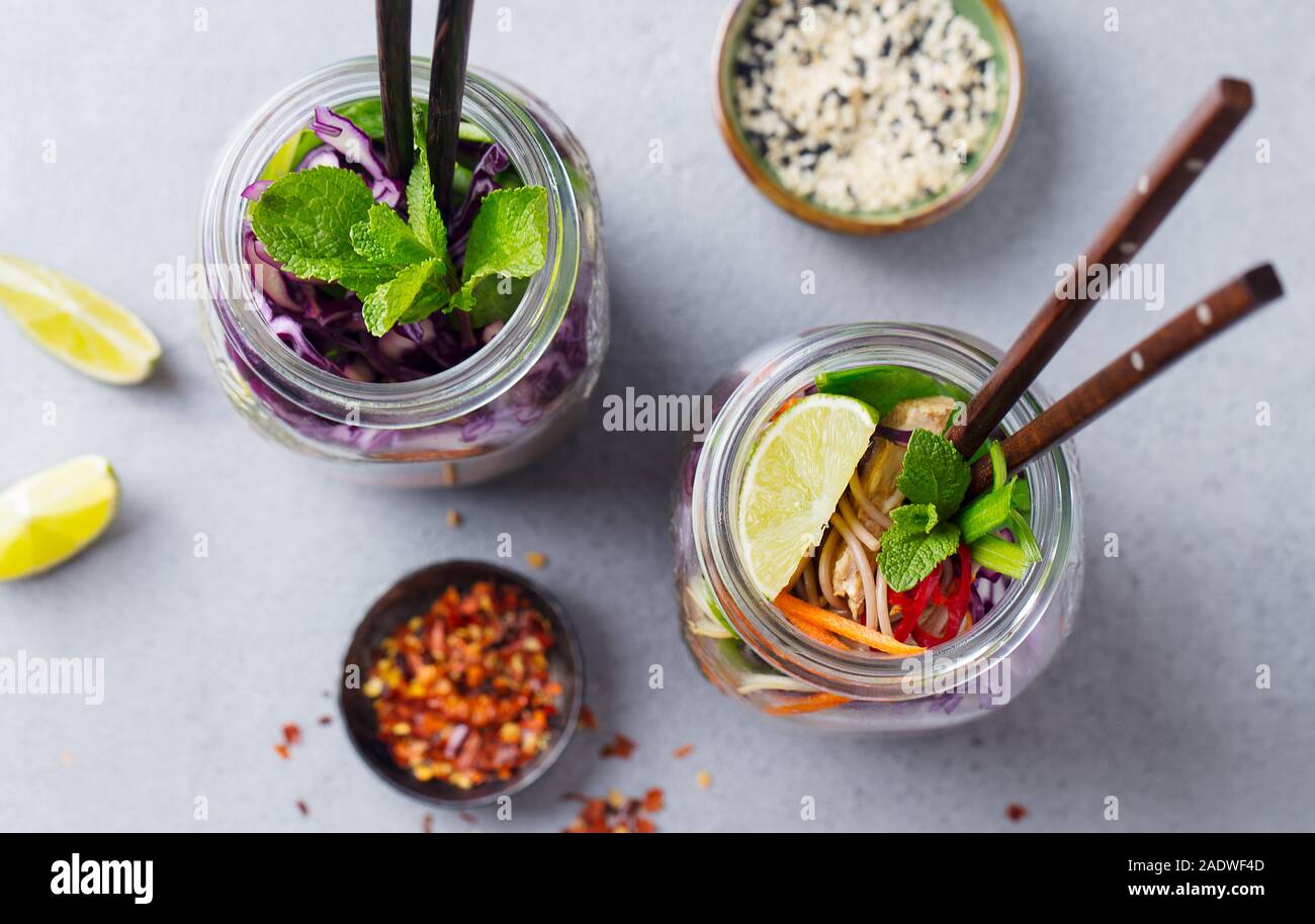 Soba Nudeln Salat, Suppe mit Gemüse, Tofu und Huhn in Gläsern. Grauer Hintergrund. Ansicht von oben. Stockfoto