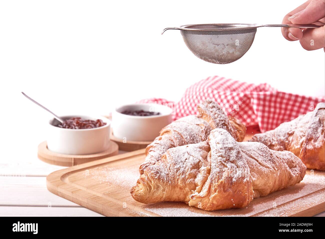 Stillleben mit Croissant und Schalen mit Marmelade. Weibliche hand mit einem Sieb und streut Zucker. Auf weissem Hintergrund. Stockfoto