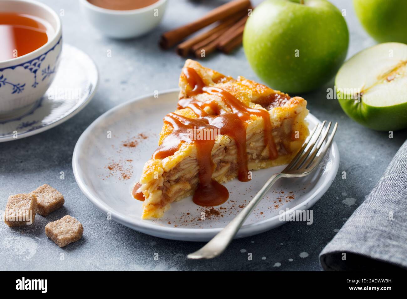 Apfelkuchen mit Karamell auf einem weißen Teller. Grauer Hintergrund. Nahaufnahme Stockfoto
