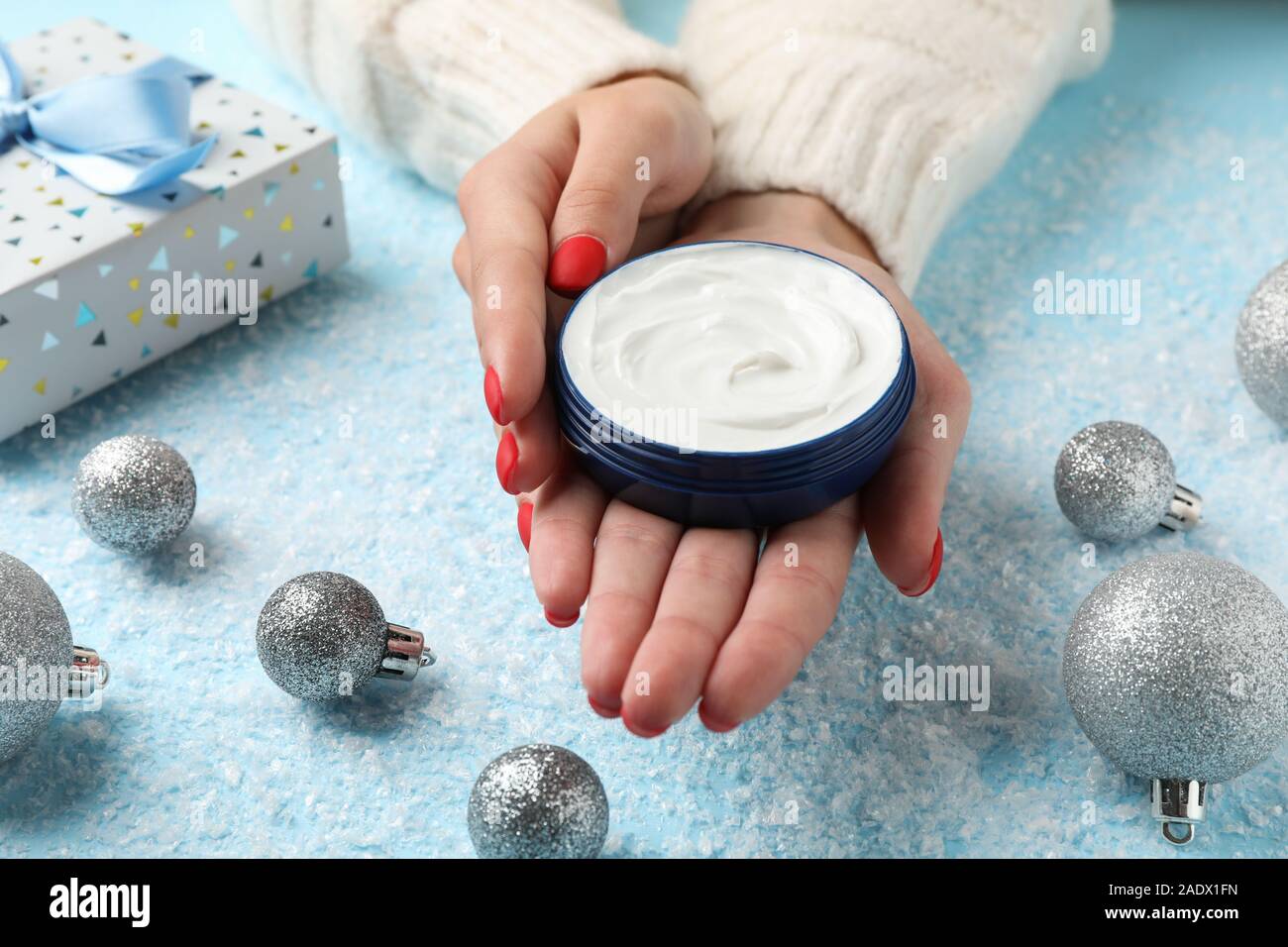 Frau in einem Pullover hält ein Glas Sahne in ihren Händen, feuchtigkeitsspendende Creme für saubere und weiche Haut im Winter, Weihnachten Spielzeug, Geschenkboxen auf verschneiten b Stockfoto