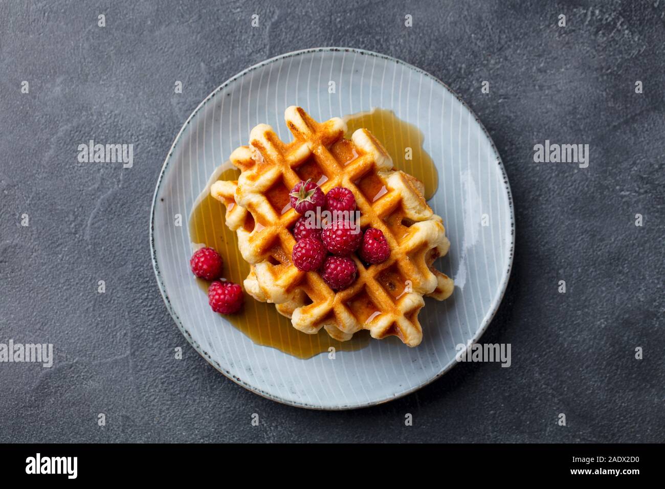 Belgische Waffeln mit Ahornsirup und frischen Himbeeren. Grauer schiefer Hintergrund. Ansicht von oben Stockfoto
