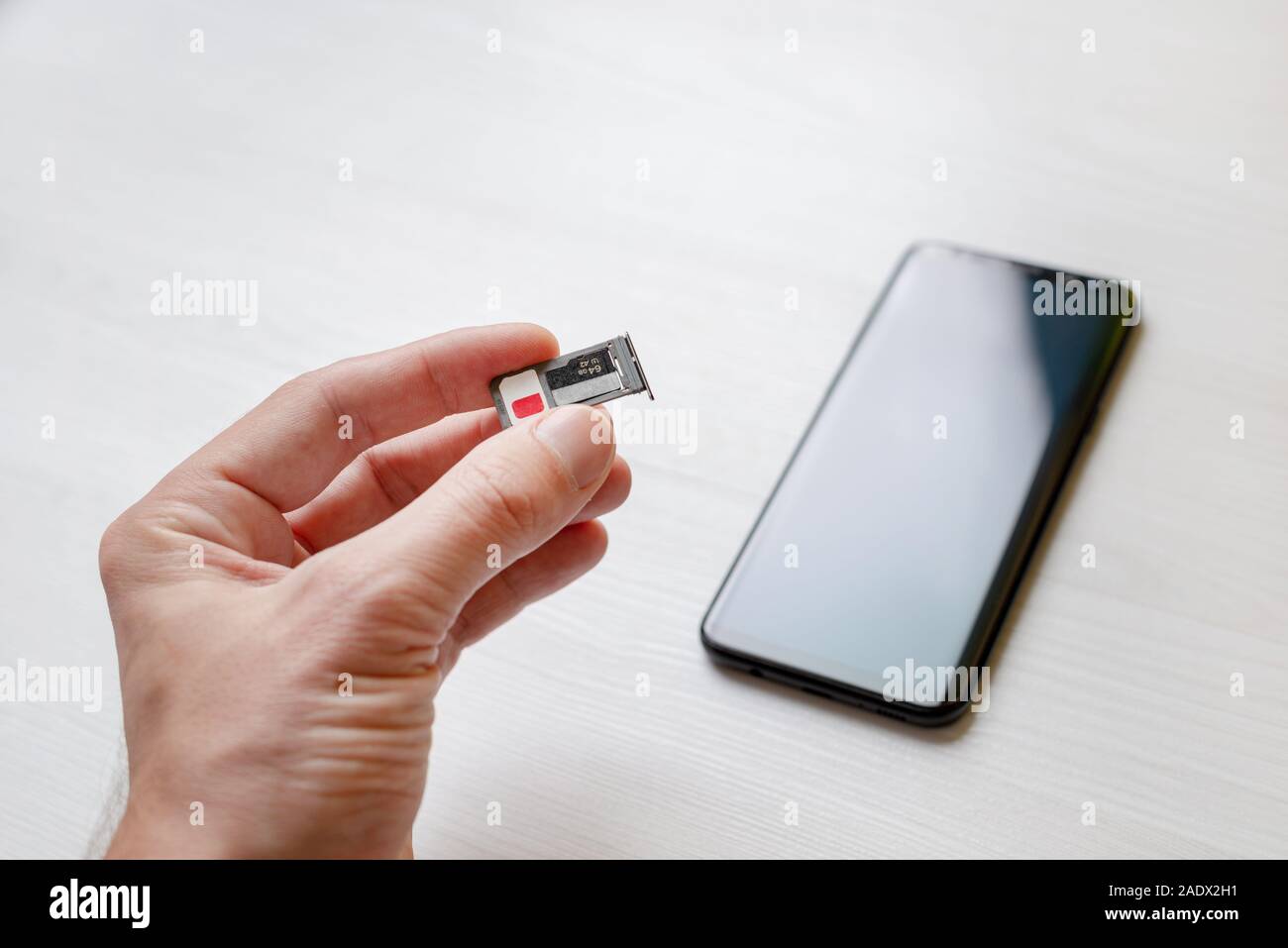 SIM-Fach Halter micro SD Card Slot Adapter in der Hand. Smart Phone im Hintergrund Stockfoto