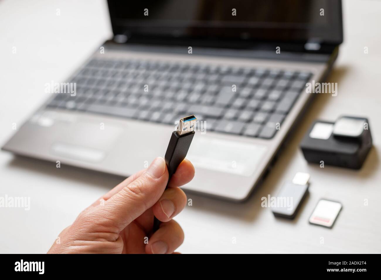 USB-Kabel in der Hand. Action Kamera und Laptop im Hintergrund. Konzept der Übertragung von Fotos und Videos. Stockfoto