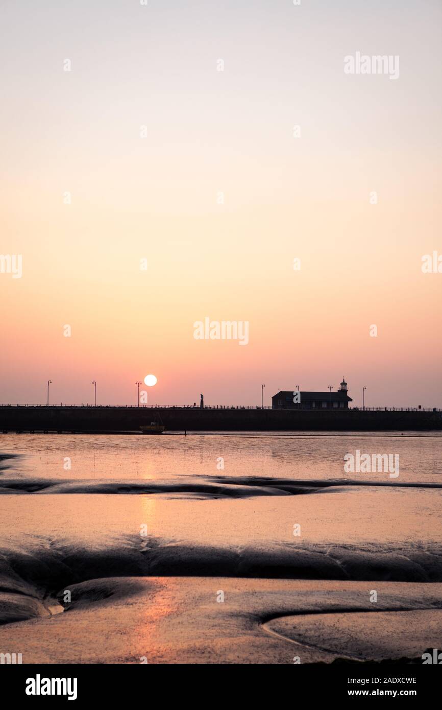 Sonnenuntergang in der Bucht von Morecambe, Lancashire, UK. Ein Blick über den Sandstrand von Morecambe Bay wie die Sonne über den steinernen Steg am Ende des Tages setzt. Stockfoto