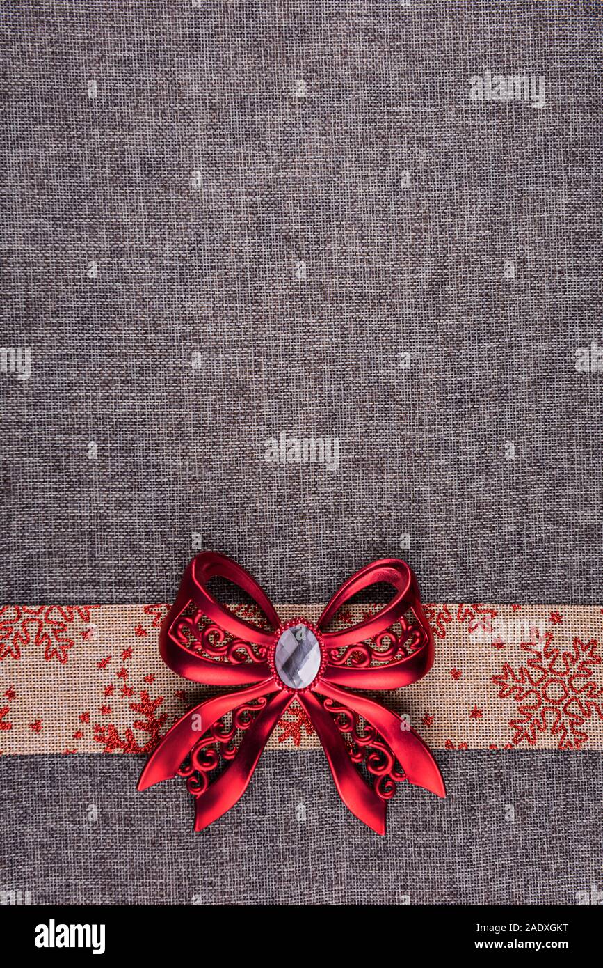 Glänzendes Rot gebunden Metallbügel auf beige Sackleinen Band mit roten Schneeflocken Ornament und auf Grau sackleinen. Vertikale Grußkarte Hintergrund w Stockfoto