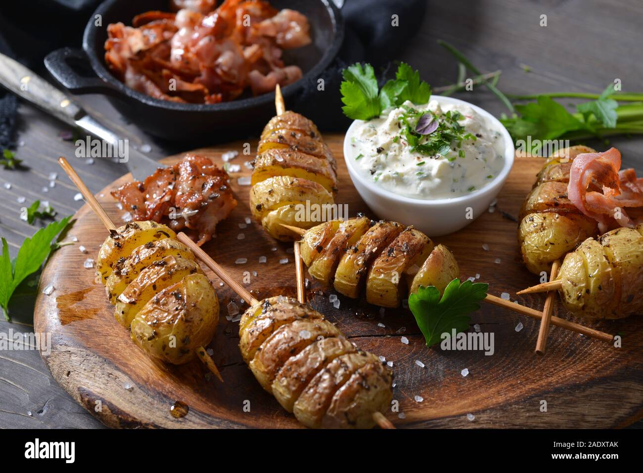 Spiralförmiger schnitt kleine Kartoffeln am Spieß gebacken mit Olivenöl und serviert mit Kraut Quark und gebratener Speck Streifen Stockfoto