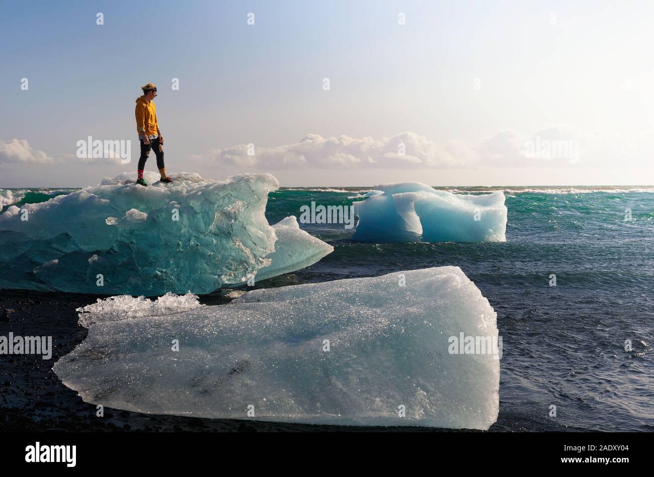 Touristische stehend auf einem Eisberg im Diamond Beach in Gletscherlagune Jokulsarlon in Island. Dieser Strand ist bekannt für seine grossen Felsen liegen auf dem Bekannten Stockfoto