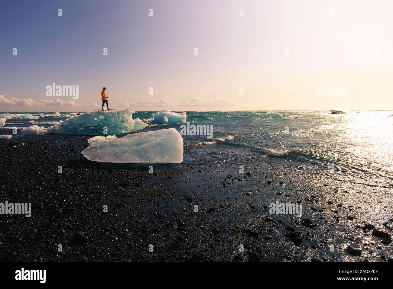 Touristische stehend auf einem Eisberg im Diamond Beach in Gletscherlagune Jokulsarlon in Island. Dieser Strand ist bekannt für seine grossen Felsen liegen auf dem Bekannten Stockfoto