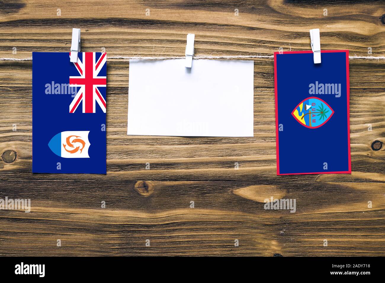 Hängenden Flaggen von Anguilla und Guam zu Seil mit wäscheklammer mit Kopie Raum befestigt auf weißem Papier auf Holz- Hintergrund. Diplomatische Beziehungen. Stockfoto