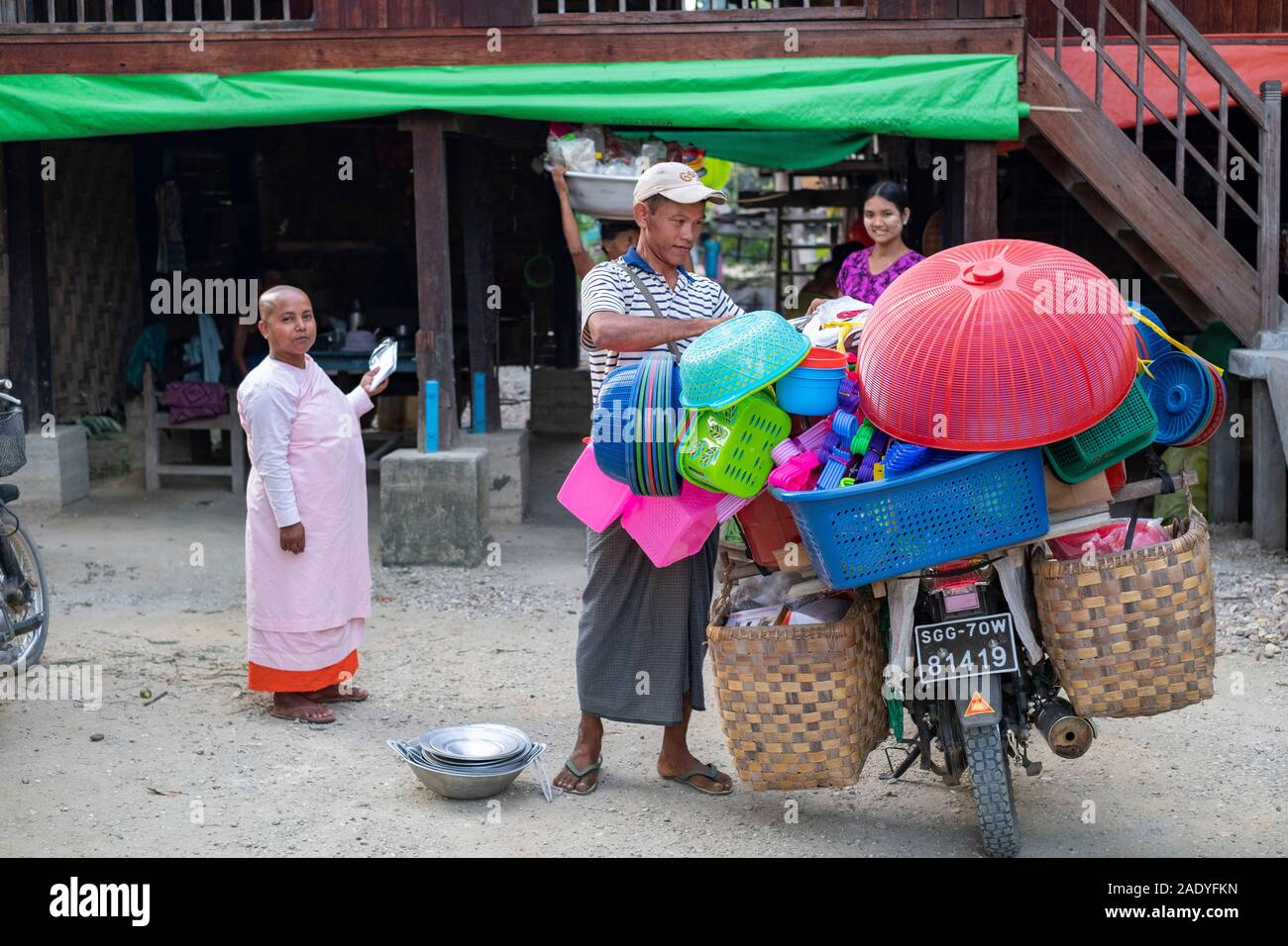 Eine burmesische Haus mit einer Vielzahl von Familie Mitglieder, darunter ein Verkäufer, seine Frau und seine Mutter vorbereiten, Waren zu verkaufen, während eine buddhistische Nonne beobachtet. Stockfoto