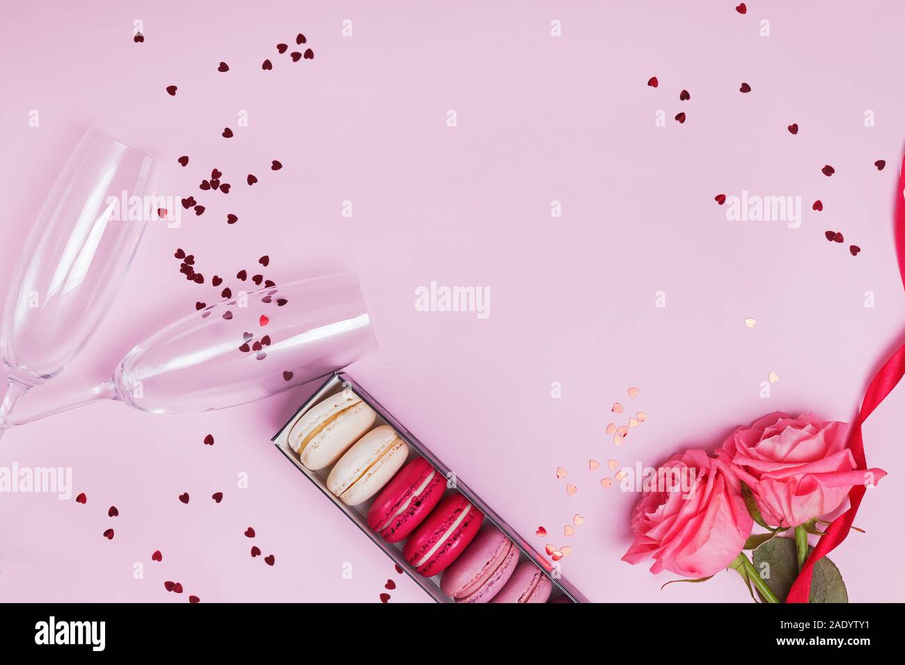 Zwei Sektgläser, Macarons, Rosen und herzförmige Konfetti auf rosa Hintergrund. Stockfoto