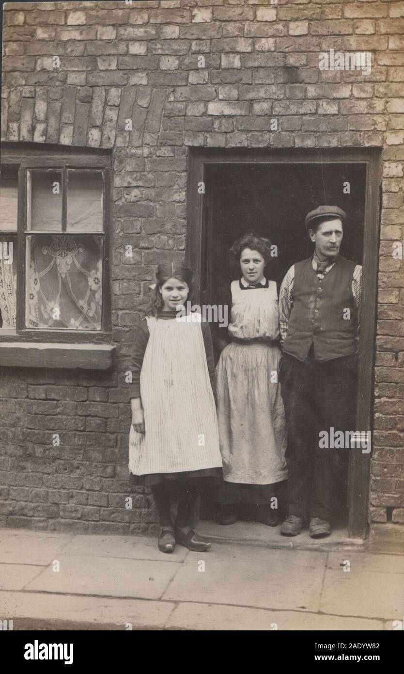 Jahrgang des frühen 20. Jahrhunderts photographische Postkarte mit einer Arbeiterfamilie Gruppe stand in der Tür Ihres bescheidenen Haus. Stockfoto