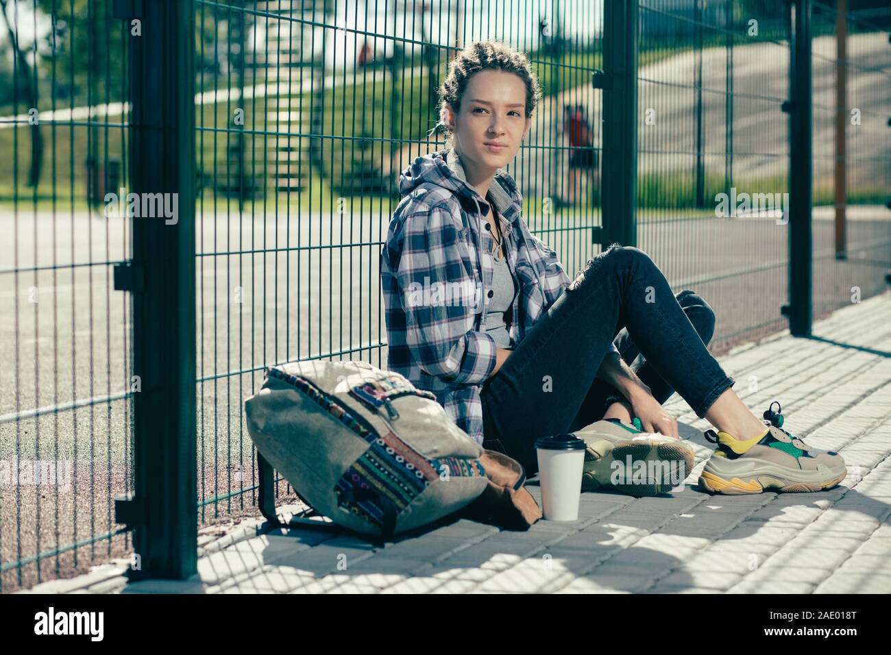 Junge Frau sitzt in der Nähe der Maschendrahtzaun mit ihren grossen Rucksack Stockfoto