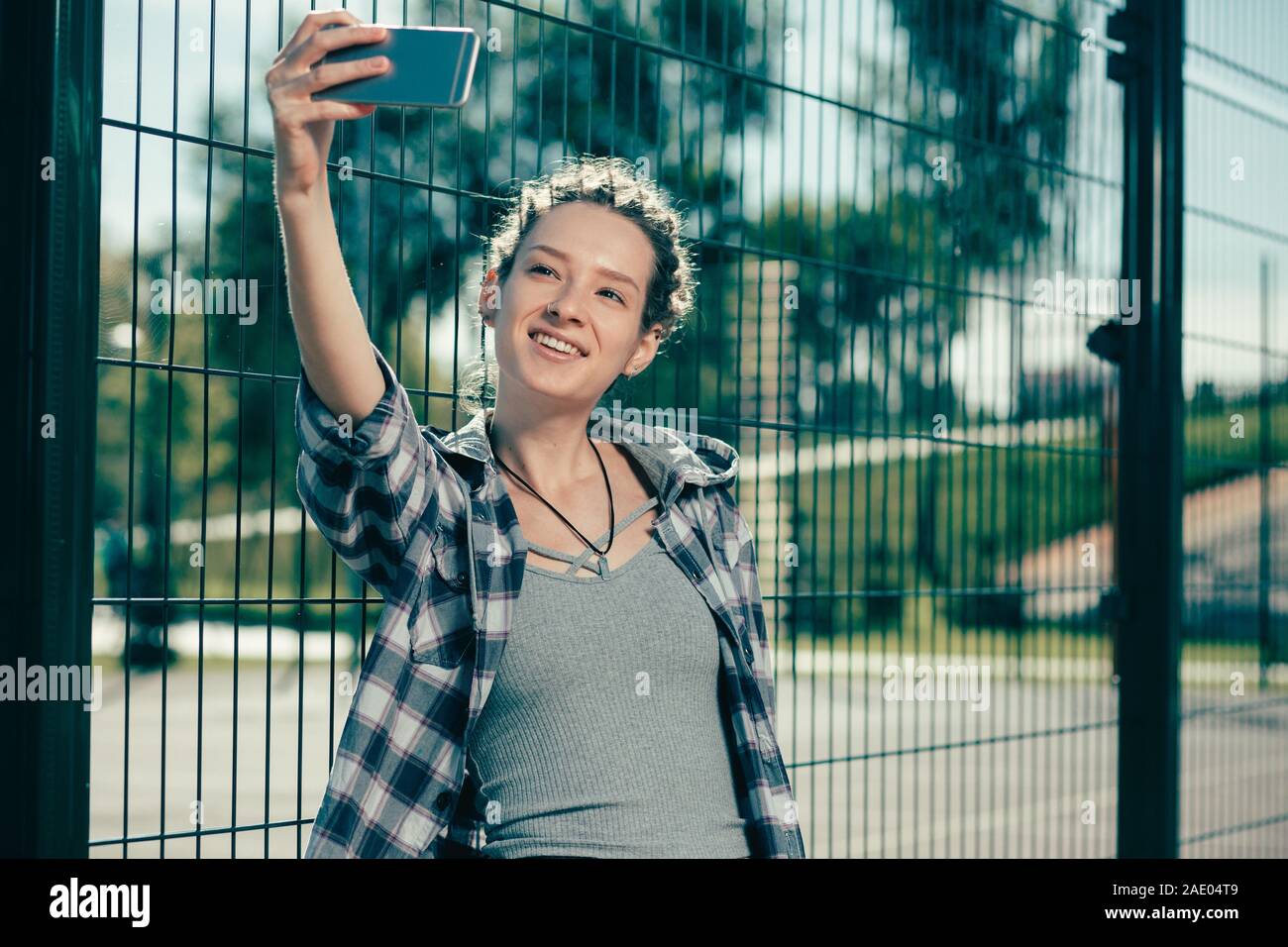 Hübsche Dame lächelnd, während Sie in der Nähe des selfies Maschendrahtzaun Stockfoto