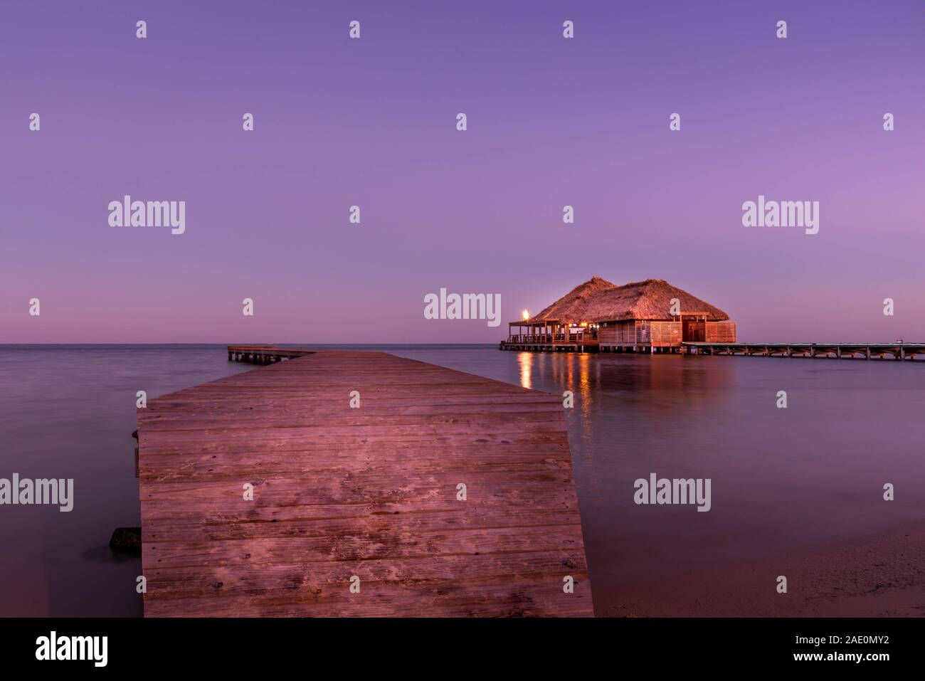 Ein wunderschön beleuchtet Overwater Bungalow mit Strohdach bei Sonnenuntergang in Ambergris Caye, Belize. Lange Belichtung Bild. Stockfoto