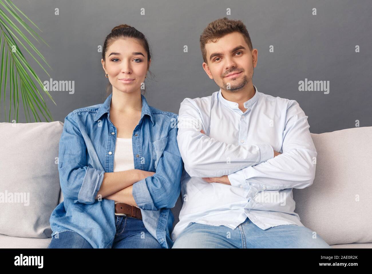 Relationnship Konzept. Junges Paar sitzt auf einem Sofa studio isoliert auf Grau verschränkte Arme lächelnd Frohe Stockfoto