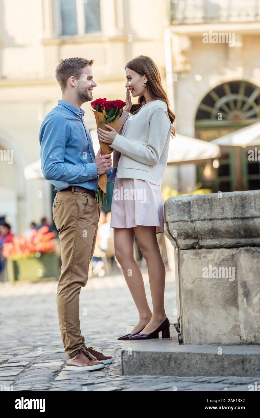 Schöner Mann, Blumenstrauß aus Rosen, glücklich zu Freundin auf der Straße Stockfoto