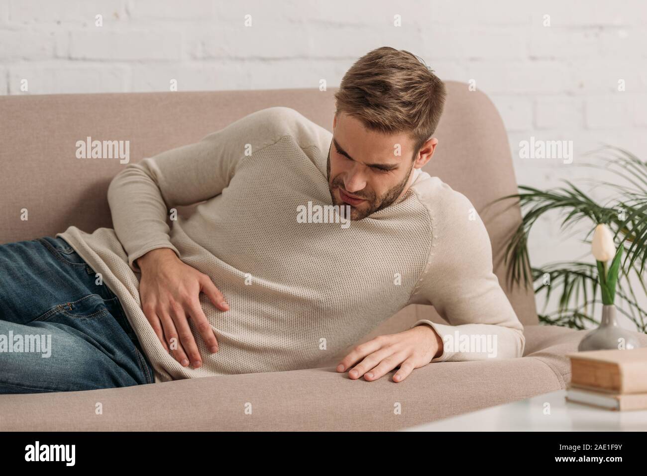 Junger Mann lag auf dem Sofa und leidet unter Bauchschmerzen Stockfoto