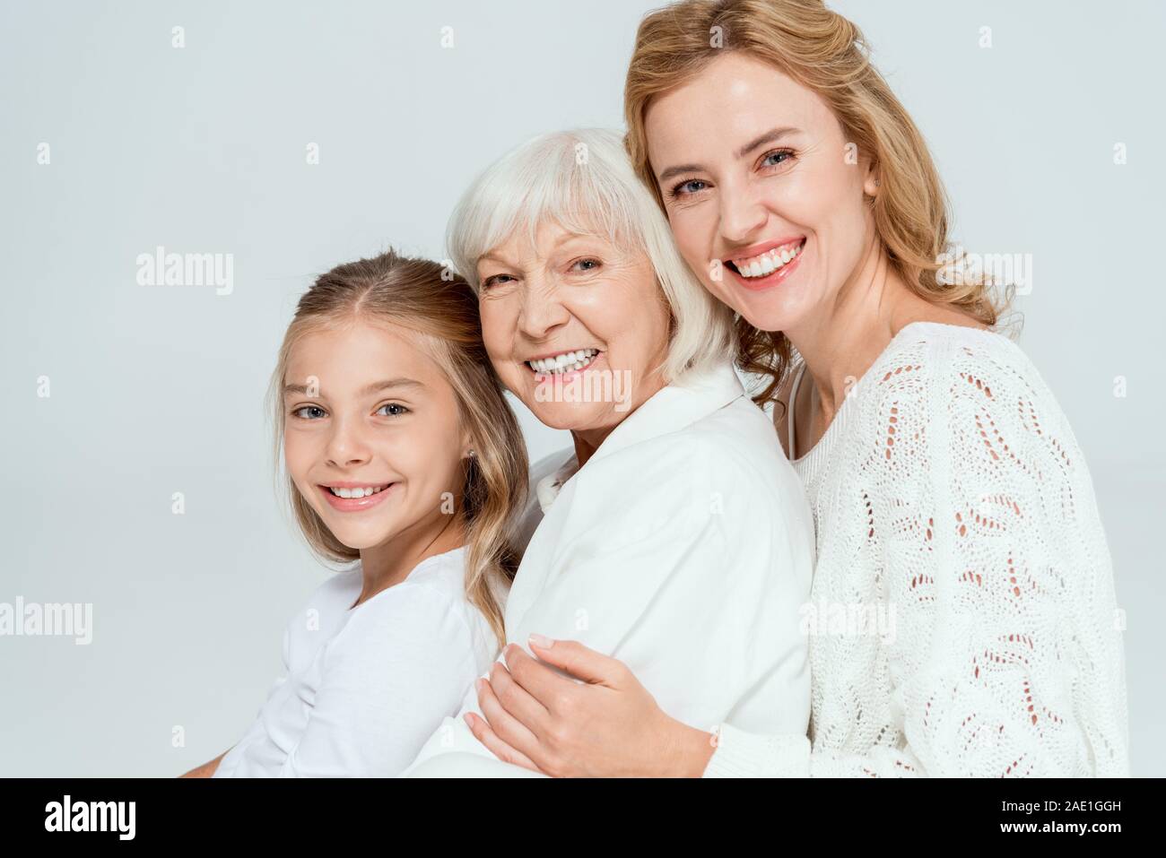 Lächelnd Enkelin, Mutter und Großmutter umarmt isoliert auf Grau Stockfoto