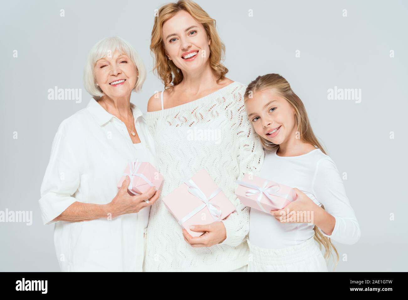 Lächelnd Enkelin, Mutter und Großmutter holding Geschenke isoliert auf Grau Stockfoto