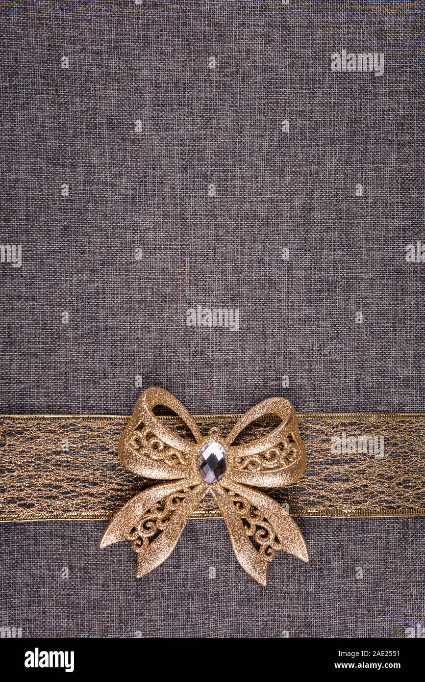 Glänzendes Band gold Glitter Bug auf Gold Farbband und auf Grau texturierte Sackleinen. Bogen und Band sind unten auf dem Bild. Vertikale Stockfoto