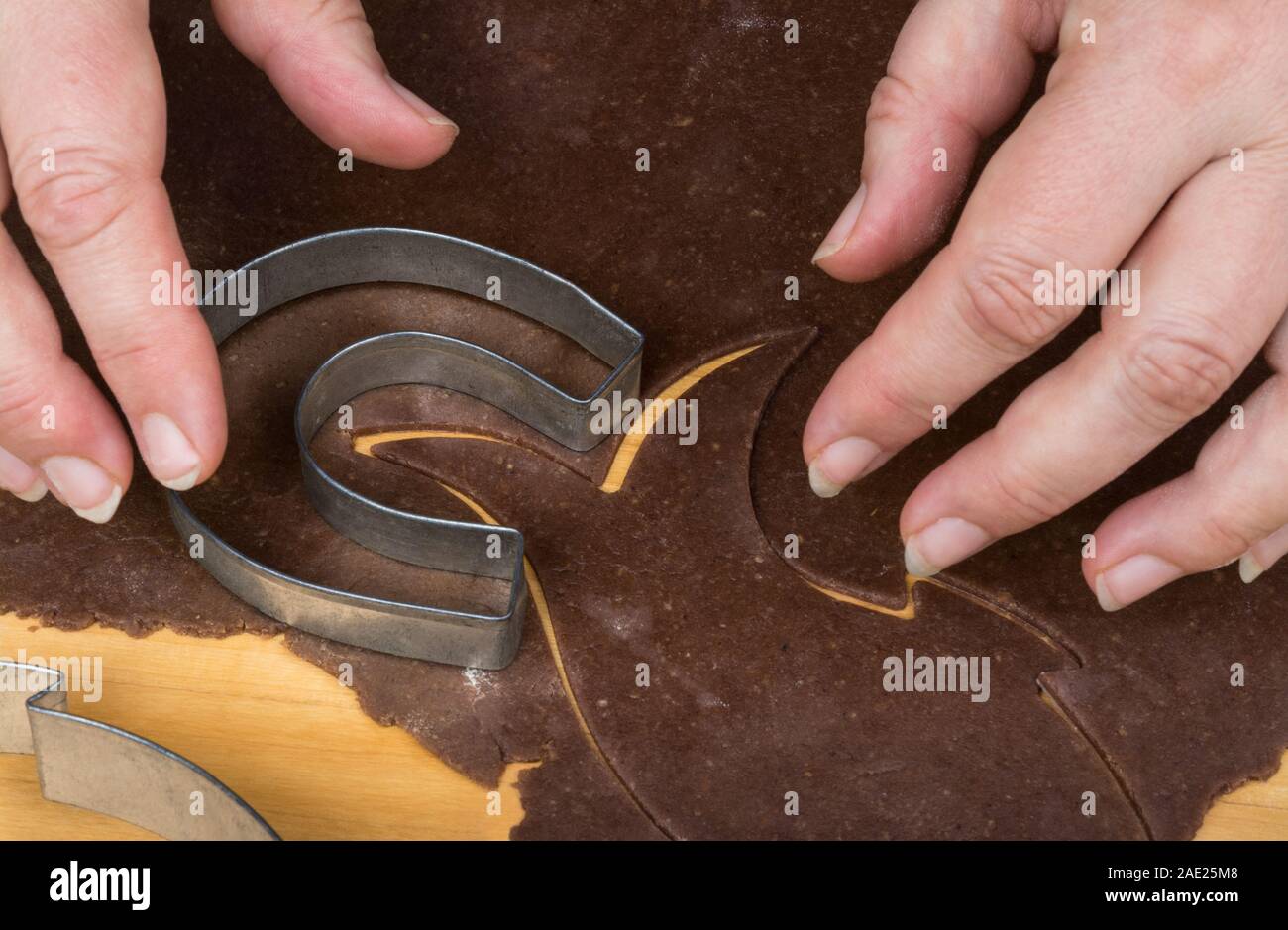 Metall 08/15 auf Lebkuchen Teig detail und weibliche Hände. Schneiden Sie eine hufeisenförmige Weihnachtsstollen aus gewalzten rohen Teig auf Holz. Stockfoto