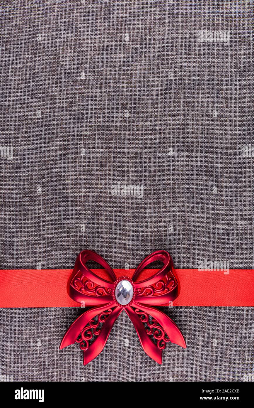 Glänzendes Rot gebunden Metallbügel auf rotem Satinband und auf Grau sackleinen Material. Vertikale Grußkarte Hintergrund mit großen Raum ein Kopieren Stockfoto
