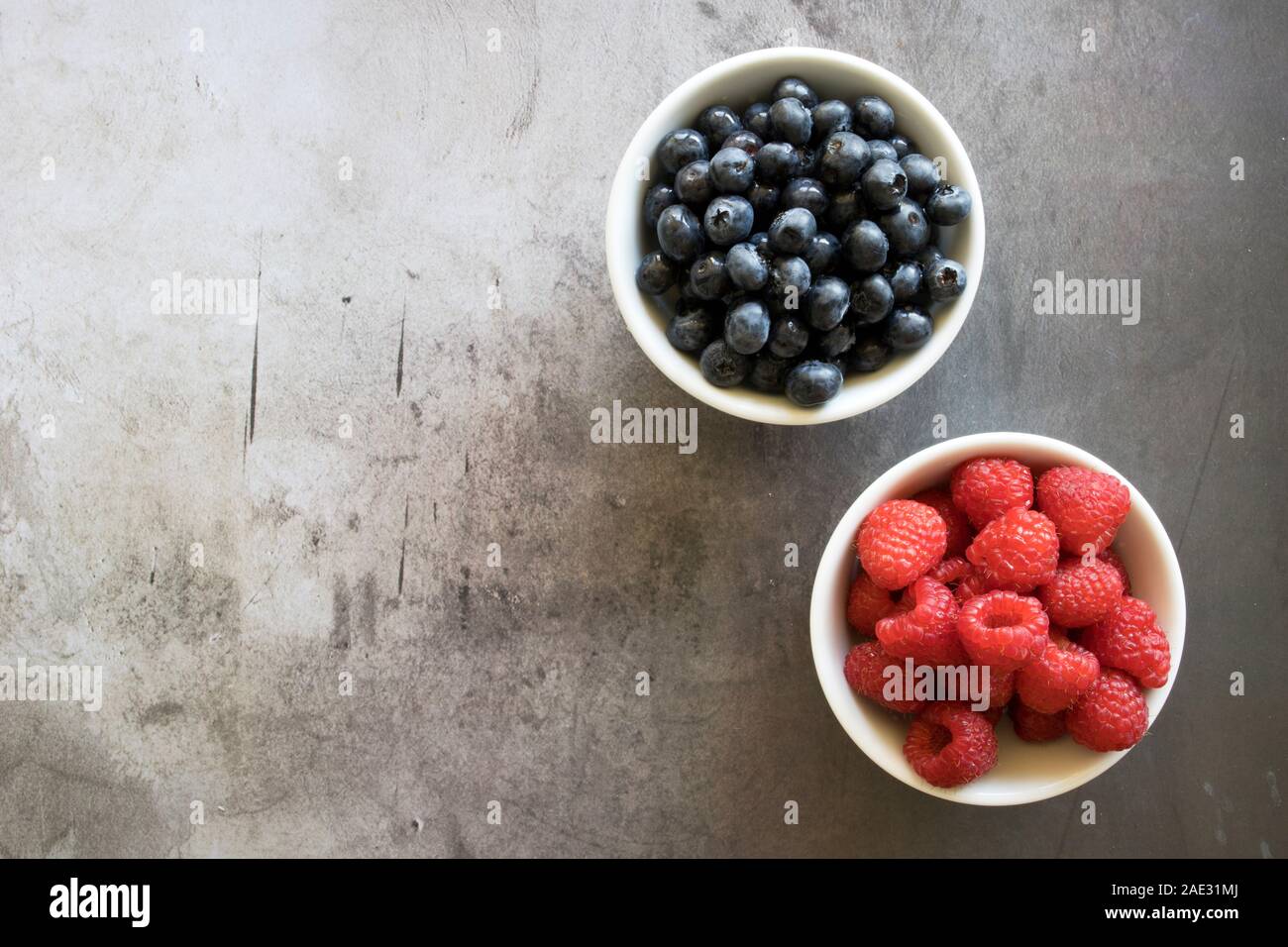 Schüssel mit Heidelbeeren und Himbeeren auf einen konkreten Hintergrund mit Raum für Kopie Stockfoto