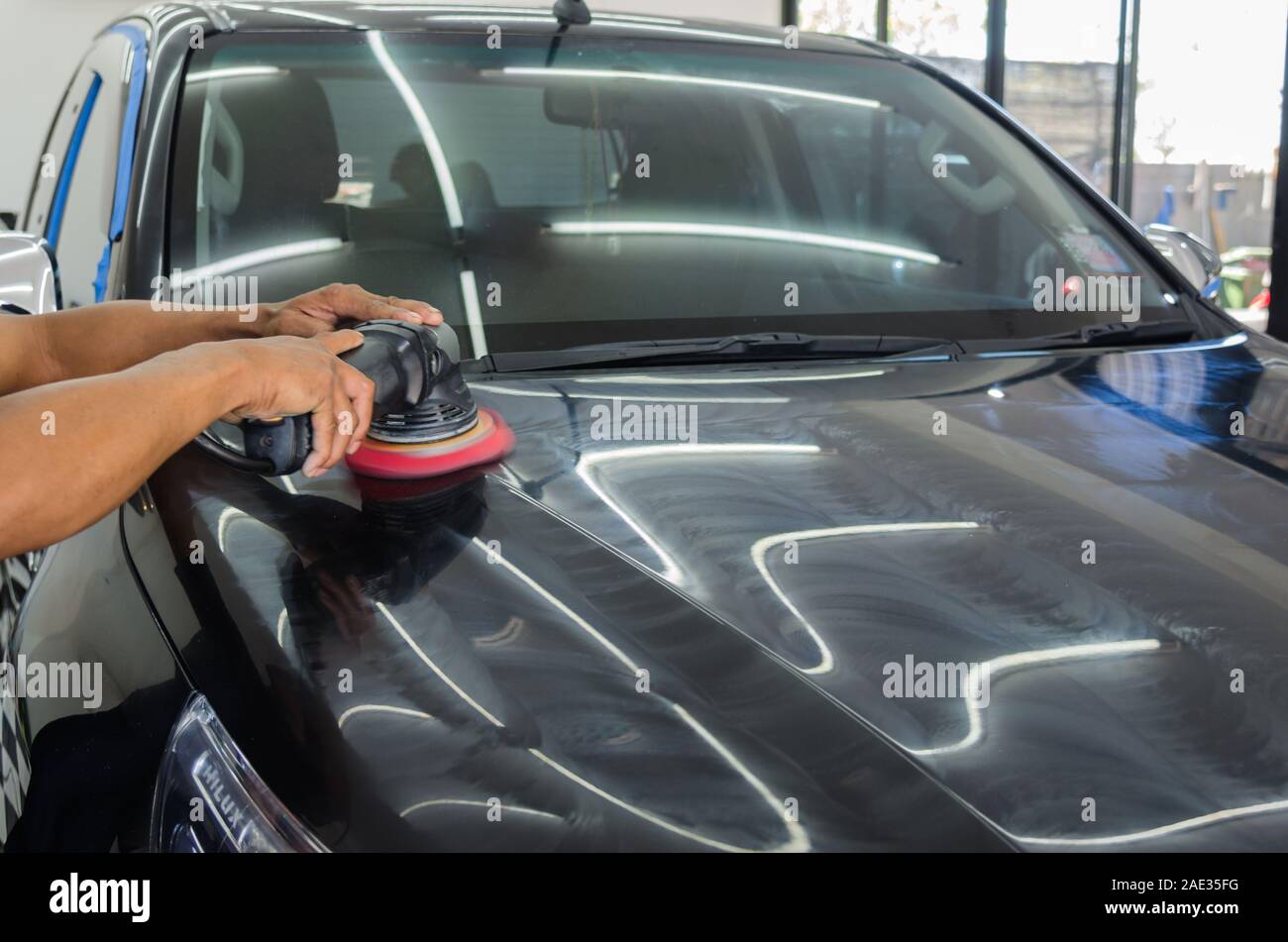 Schwarzes auto Kratzer entfernen. Ein Mann hält ein Auto polieren Werkzeug in der Garage Stockfoto