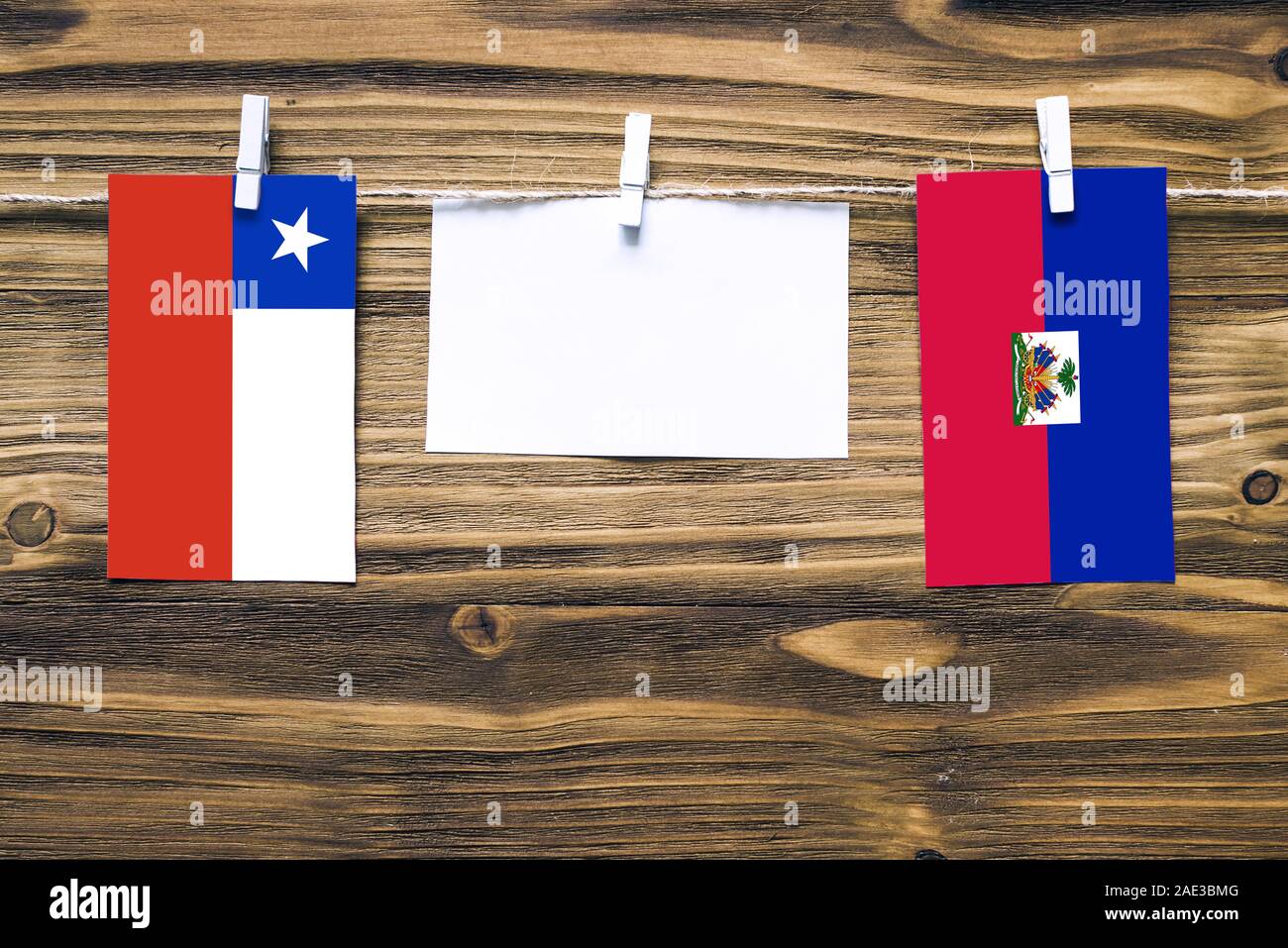 Hängenden Flaggen von Chile und Haiti zu Seil mit wäscheklammer mit Kopie Raum befestigt auf weißem Papier auf Holz- Hintergrund. Diplomatische Beziehungen zw. Stockfoto